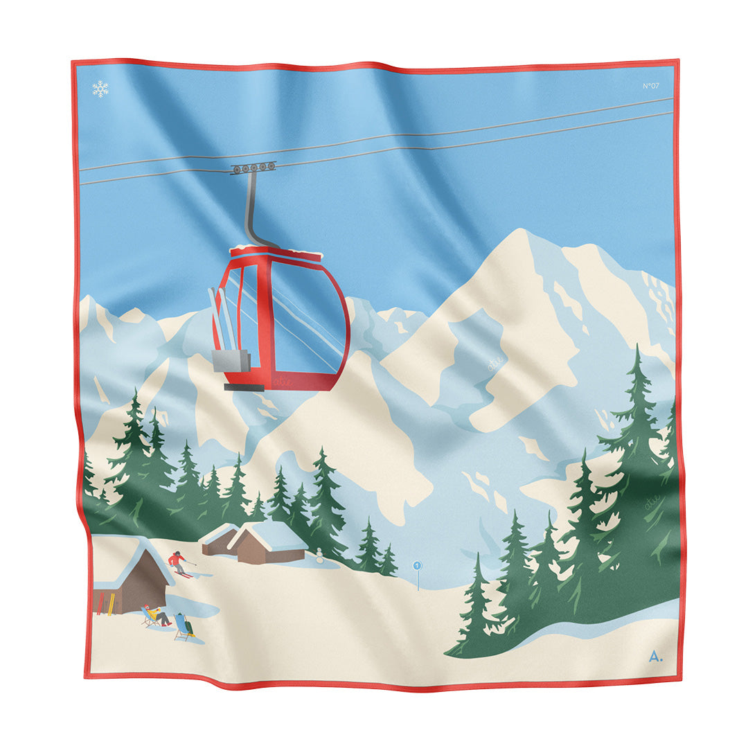 Das Bild zeigt ein Seidentuch ausgebereitet. Zu sehen ist eine Winterlandschaft mit Bergen, blauem Himmel, Skipiste, Gondel in den Farben rot, weiß, blau und grün. Handrollierter roter Saum